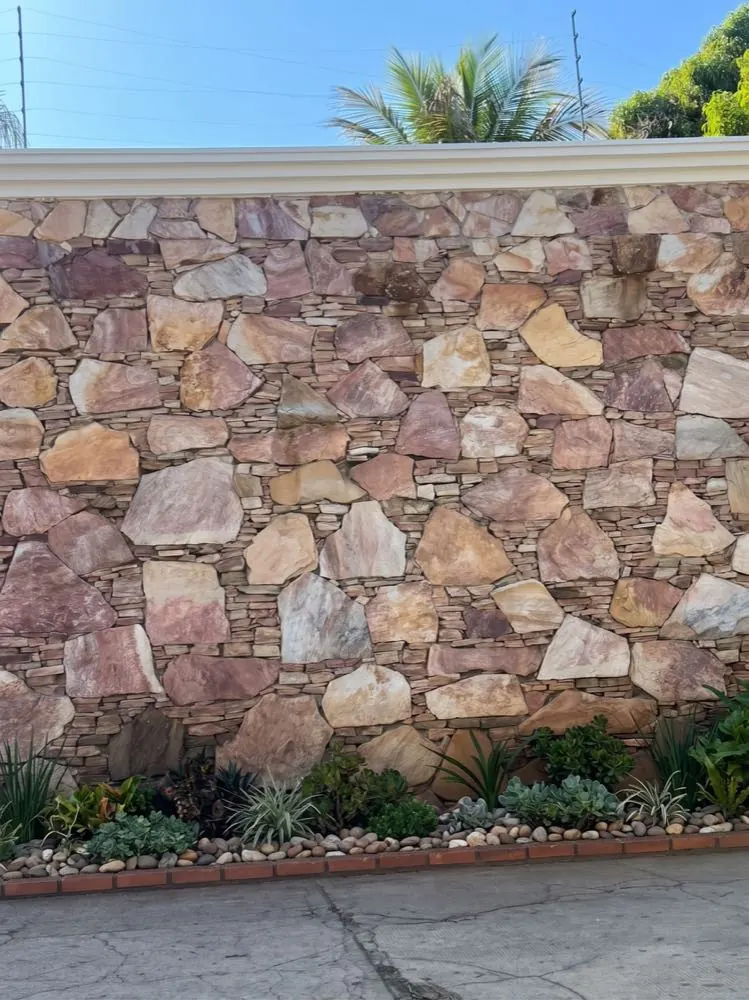 Muro revestido com lajinha irregular de Pedra Ouro Preto e paisagismo na base